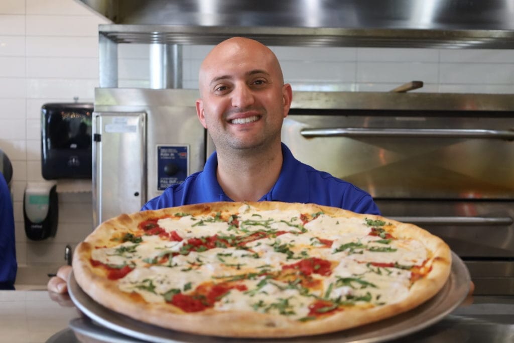 Asaro's Pizzeria team member holding a fresh whole pizza in the Sarasota kitchen, ready for catering and group orders