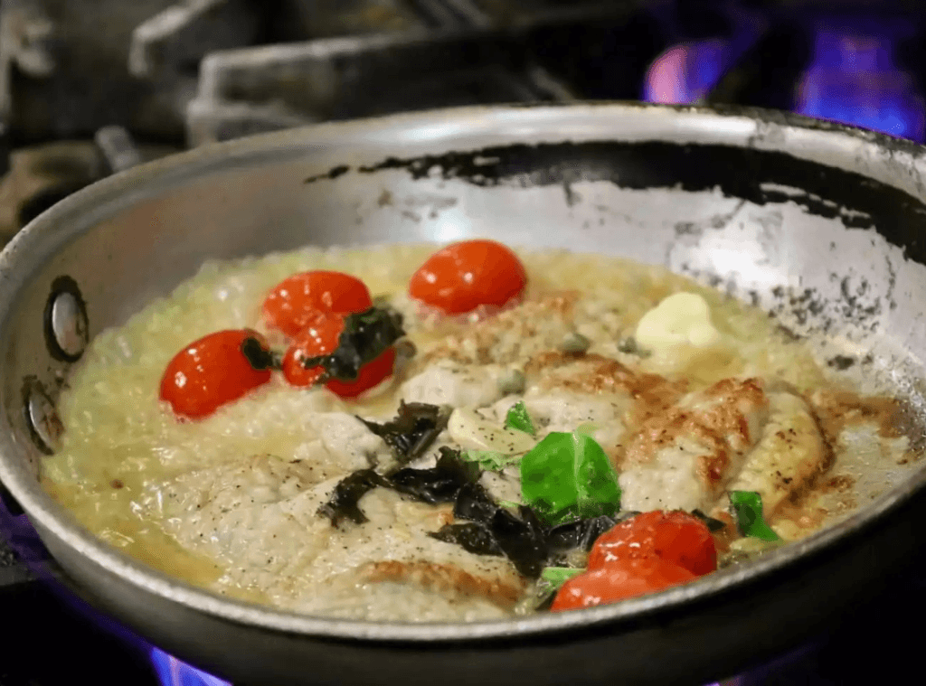 Seared chicken with cherry tomatoes, fresh basil, and a white wine butter sauce cooking in a pan at Asaro's Pizzeria Italian kitchen in Sarasota